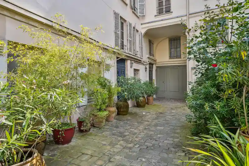 Cour intérieure pavée d'un immeuble parisien avec végétation luxuriante